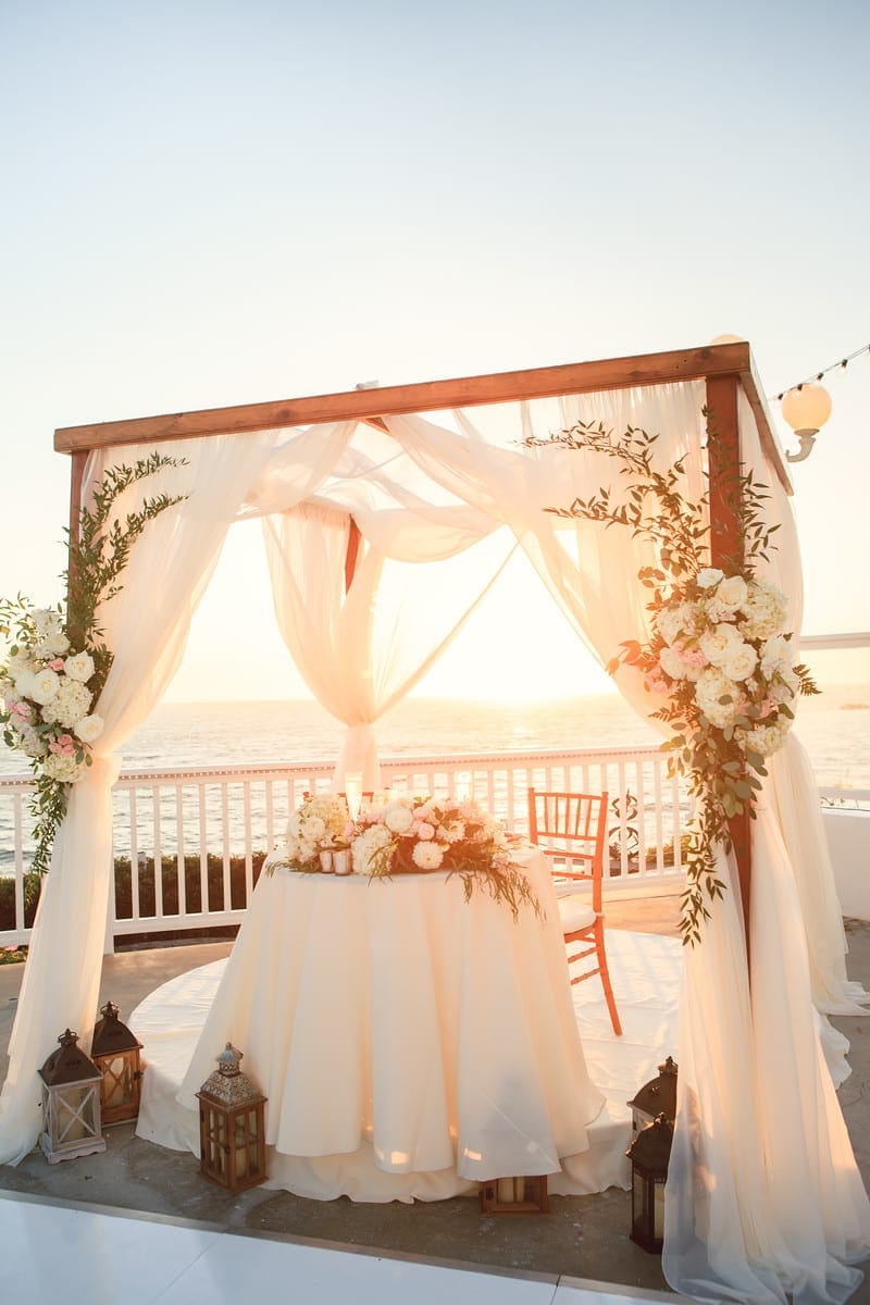 A breathtaking wedding ceremony set up on the sandy beach of Laguna Beach, southern California, bathed in the warm hues of a picturesque sunset.
