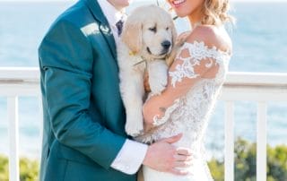 A bride and groom posing with their golden retriever at a picturesque Southern California beach.