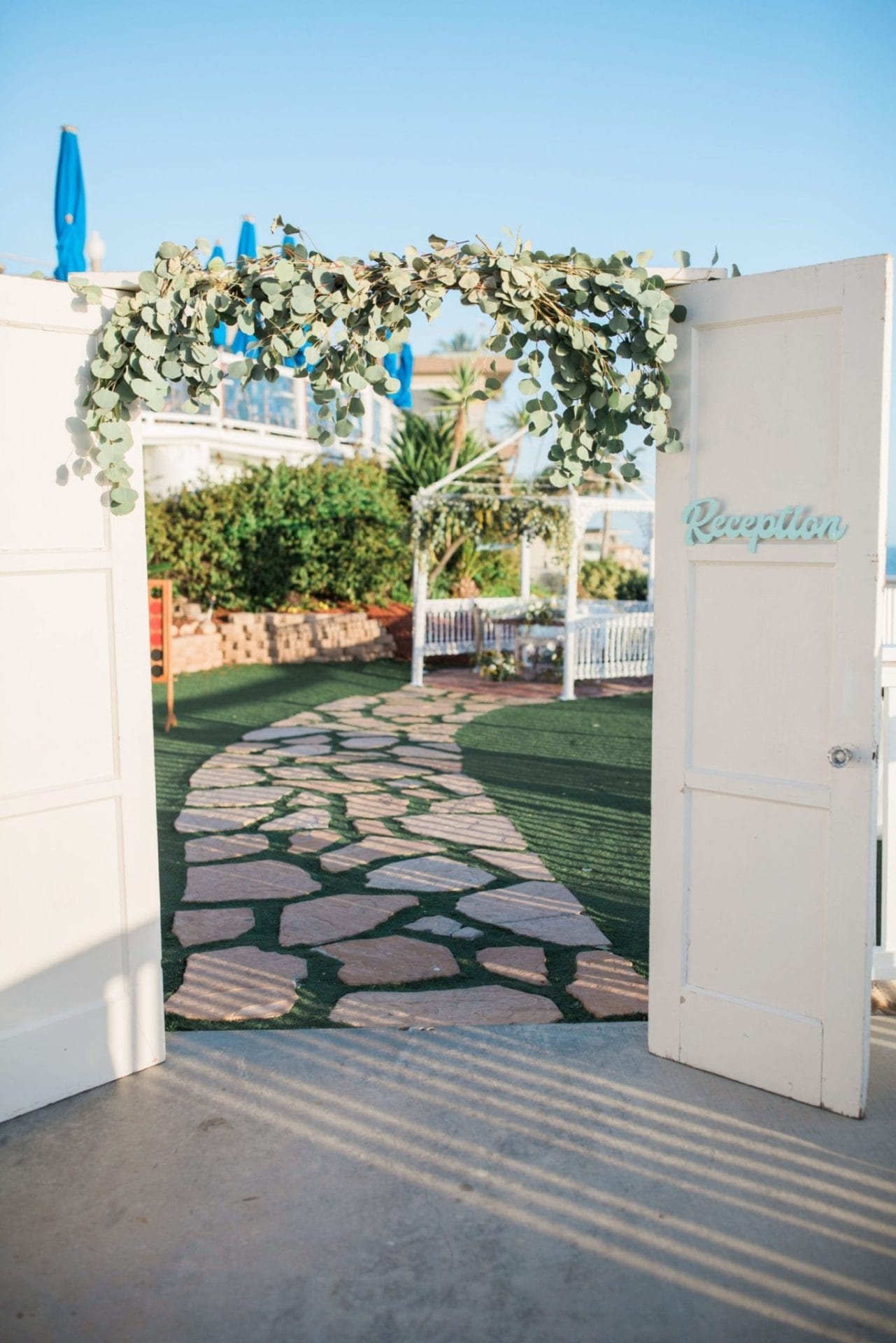 A white door with a pathway leading to a beach wedding at one of the best southern CA wedding venues.