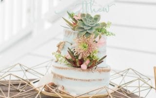 A wedding cake adorned with succulents on top of a rustic wooden table, set in a charming southern California wedding venue.