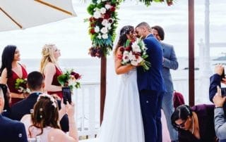 A bride and groom kissing under an arch at their romantic wedding ceremony in one of the stunning Laguna Beach wedding venues.
